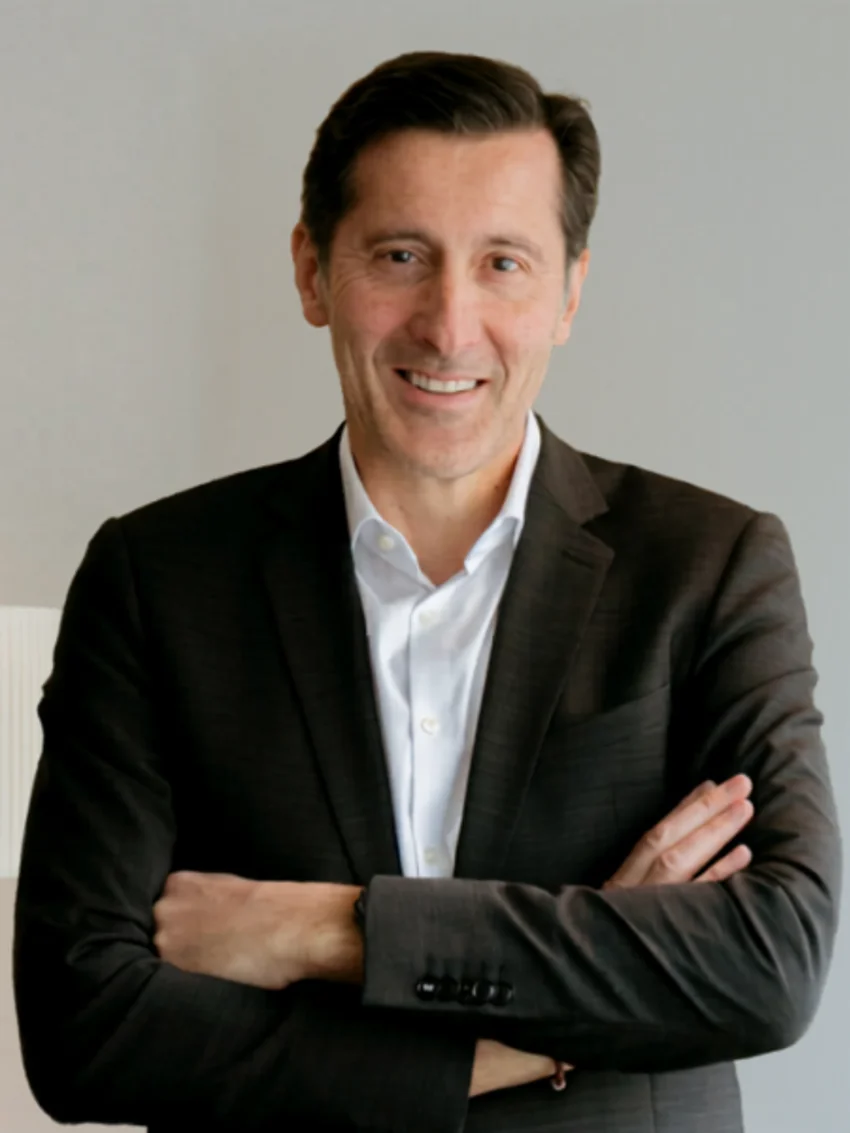 Photo de profil professionnelle d’une personne en tenue formelle, bras croisés, sur fond intérieur minimaliste.