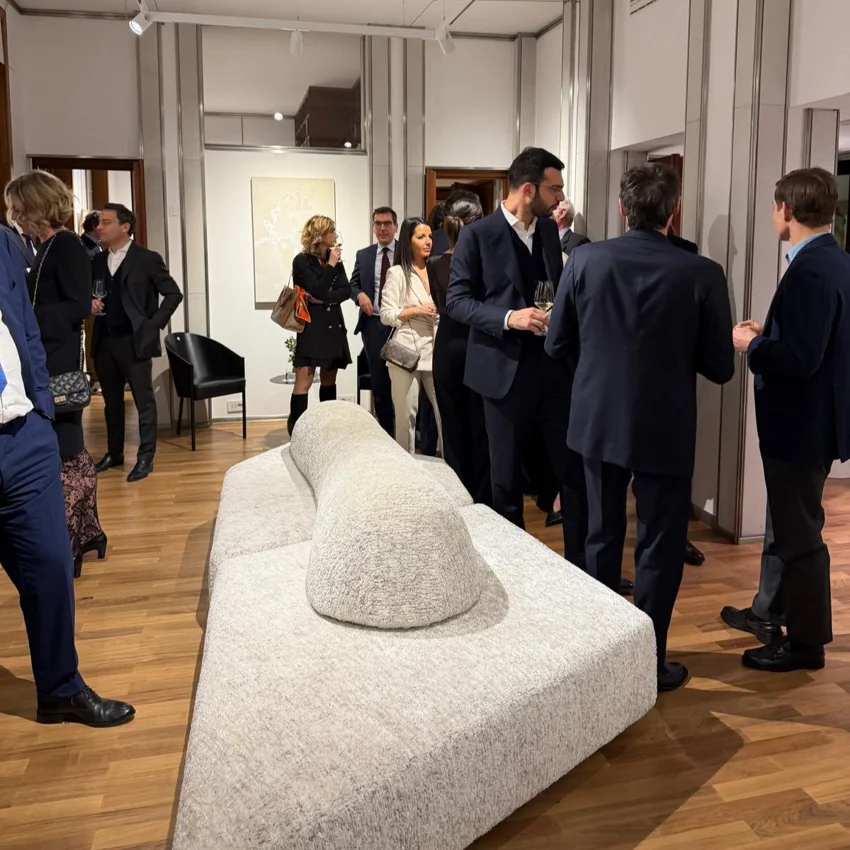 Événement professionnel dans un showroom design avec invités en tenue formelle autour d’un canapé moderne.